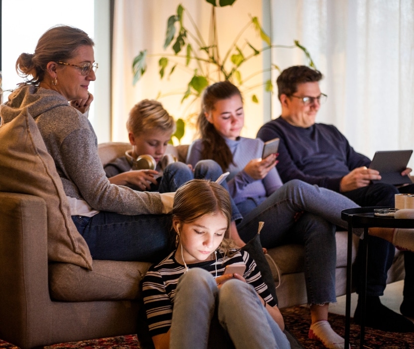 A family of four sits on the couch, each watching online streaming on their own device.